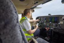 A pilot in an aircraft cockpit, focused on operating controls on the control panel