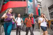 Group of male and female students walk out of The George building chatting and smiling after a class