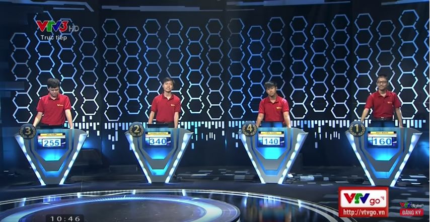 Four contestants in red shirts stand in front of podiums on a TV game show set
