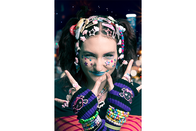 Portrait of a person with colourful star stickers, bold makeup, hair accessories and beaded jewellery.