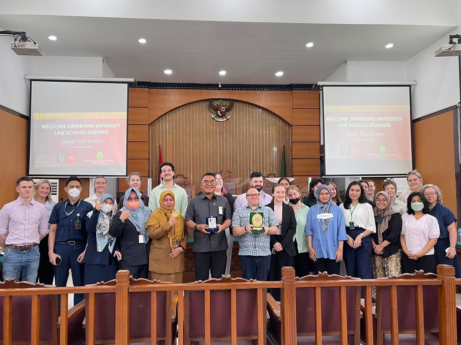 A group of students and staff stand in an Indonesian court room