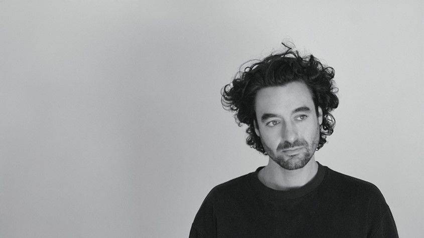 A black and white headshot of Kieran, in a black t-shirt and gazing off camera.