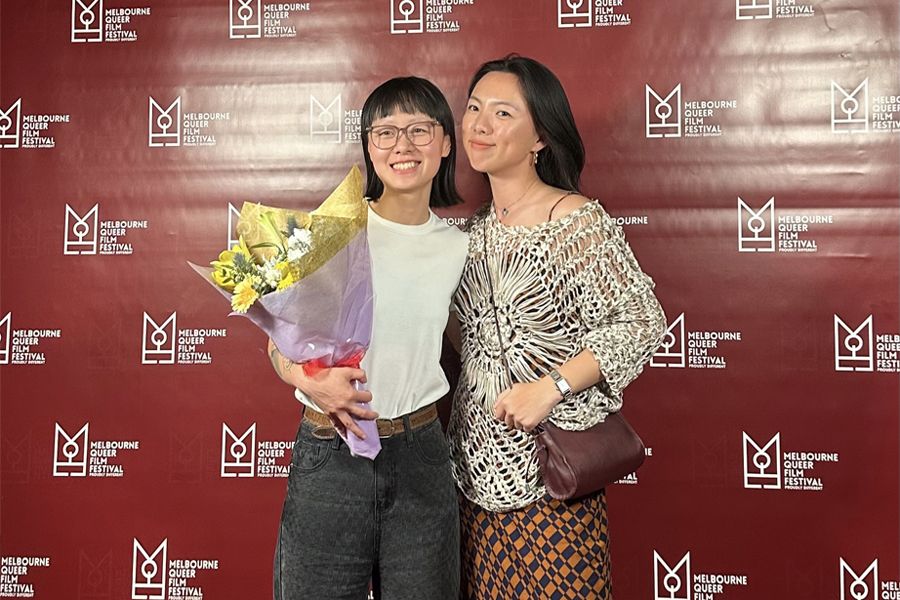 Two young women (left, holding flowers) standing together smiling at the camera 