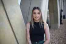 Mid shot of woman outdoors leaning against wall facing camera