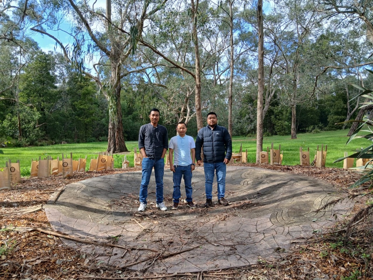 Three male students stand in the center of a traditional aboriginal fire pit.