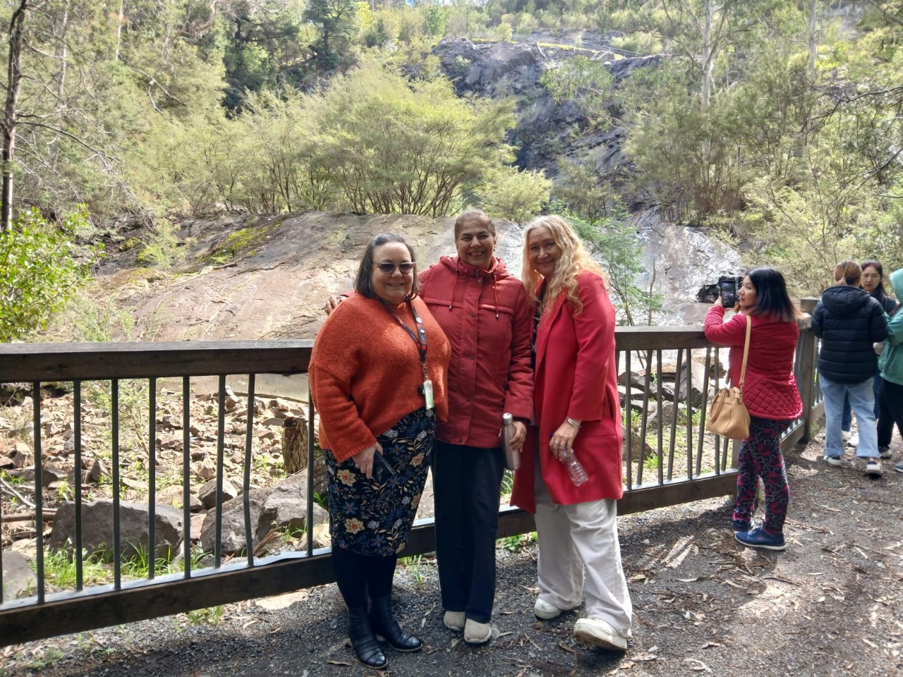  Elder-in-Residence Miranda Madgwick stands with two Swinburne Migrant English students in front of a beautiful view of trees and water at the Maroondah Reservoir.