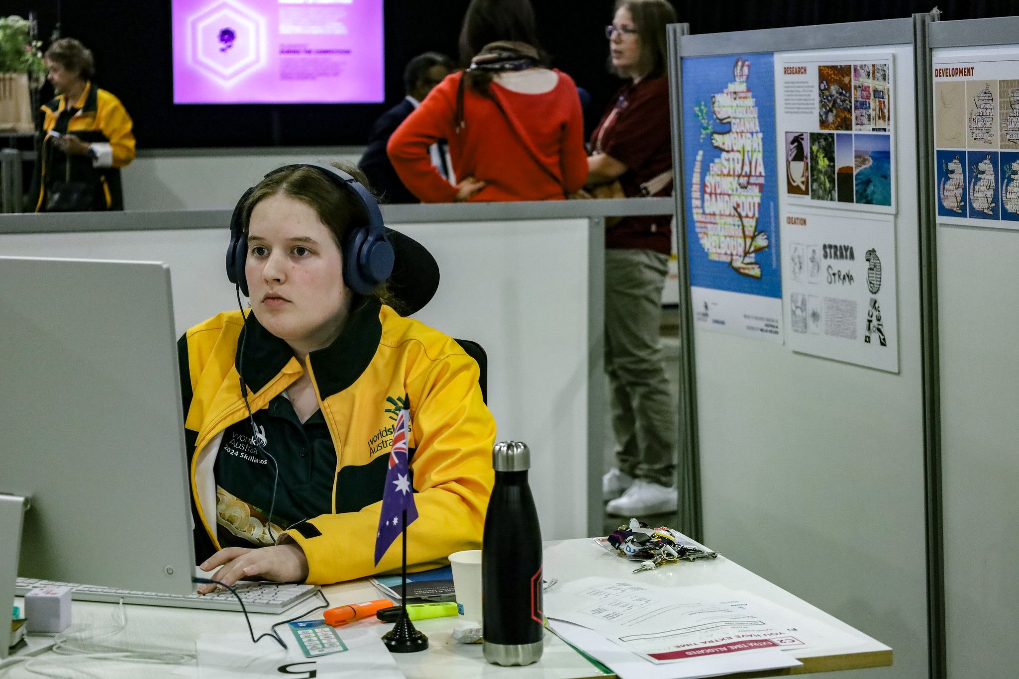 Nellie Holder sitting at a computer. She is wearing a yellow "Skillaroos" jacket and headphones. She is concentrating intently. 