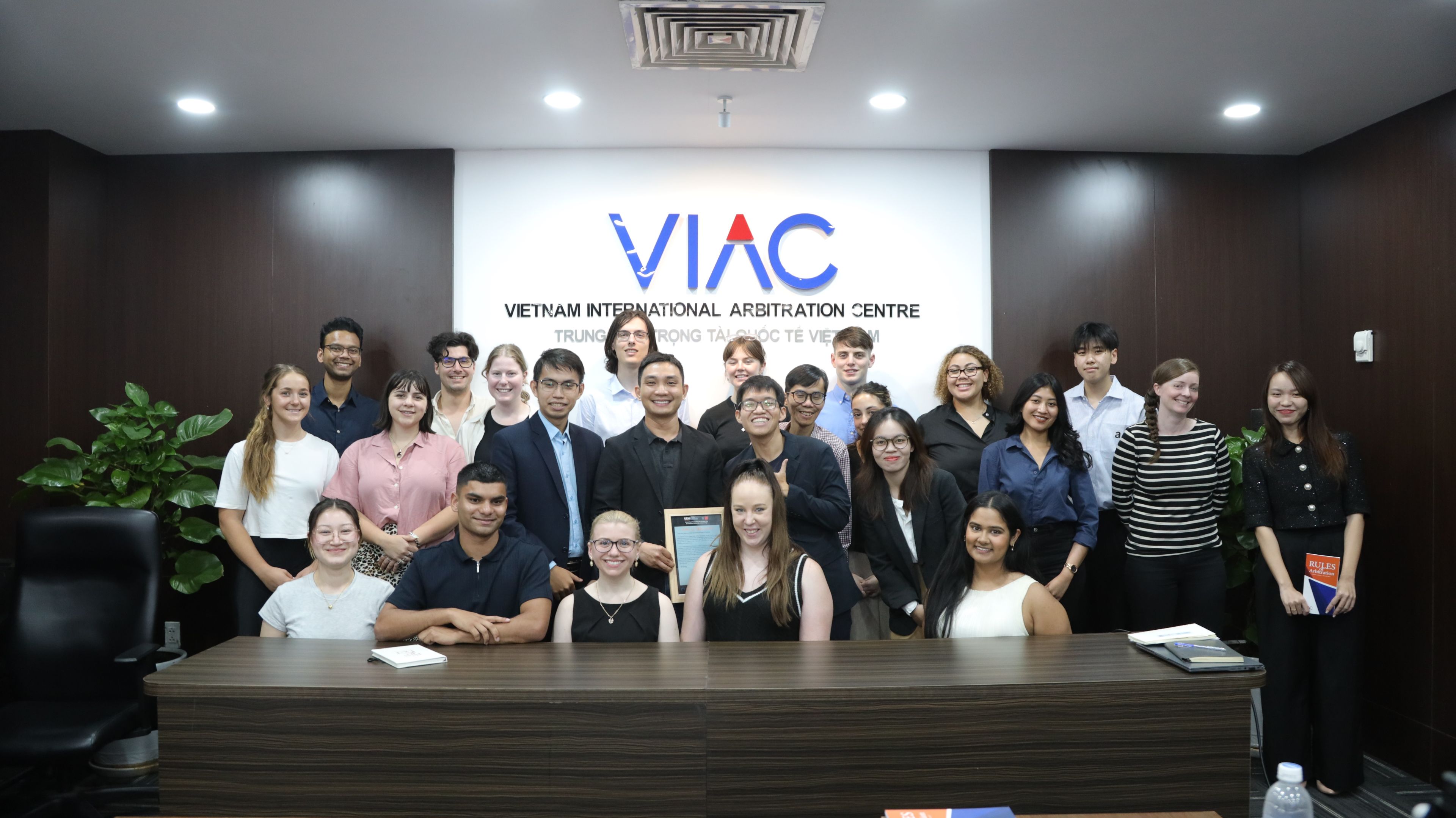 A group of students and staff in a contemporary office with the Vietnam International Arbitration Centre logo on the wall behind them