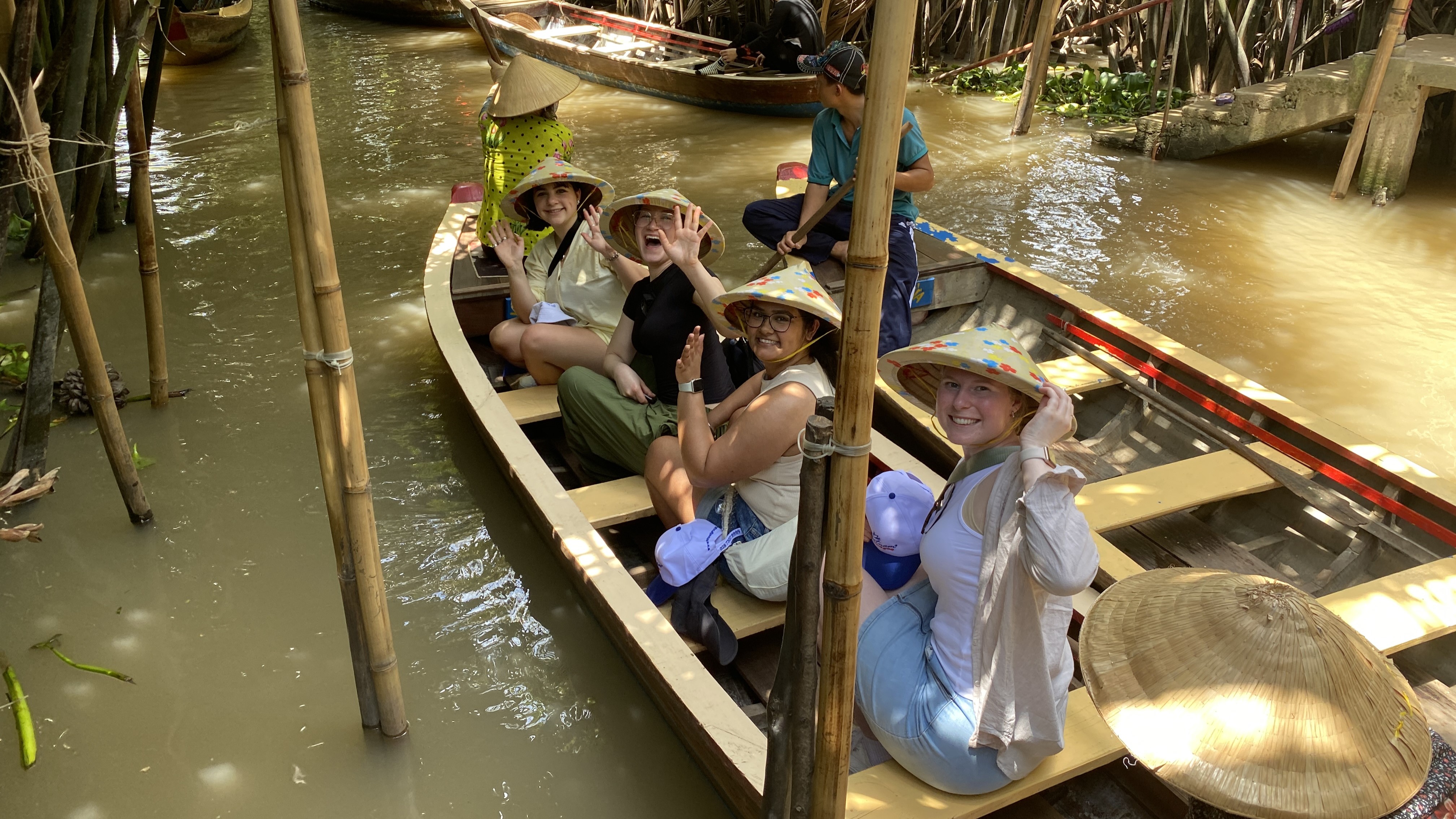 Four students wave excitedly as they ride in a Vietnamese basket boat 