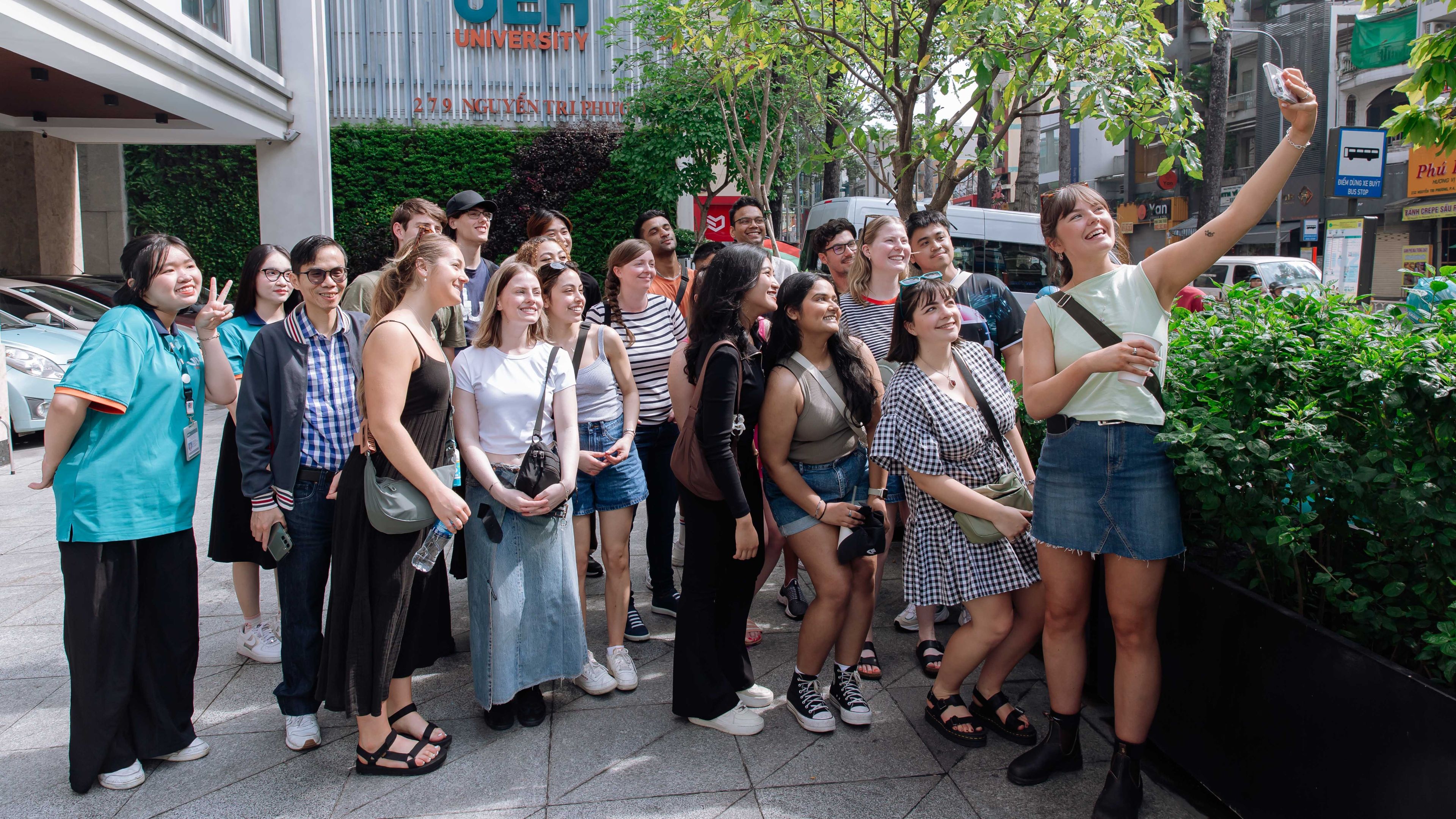 A large group pf students pose for a selfie outside the UEH campus