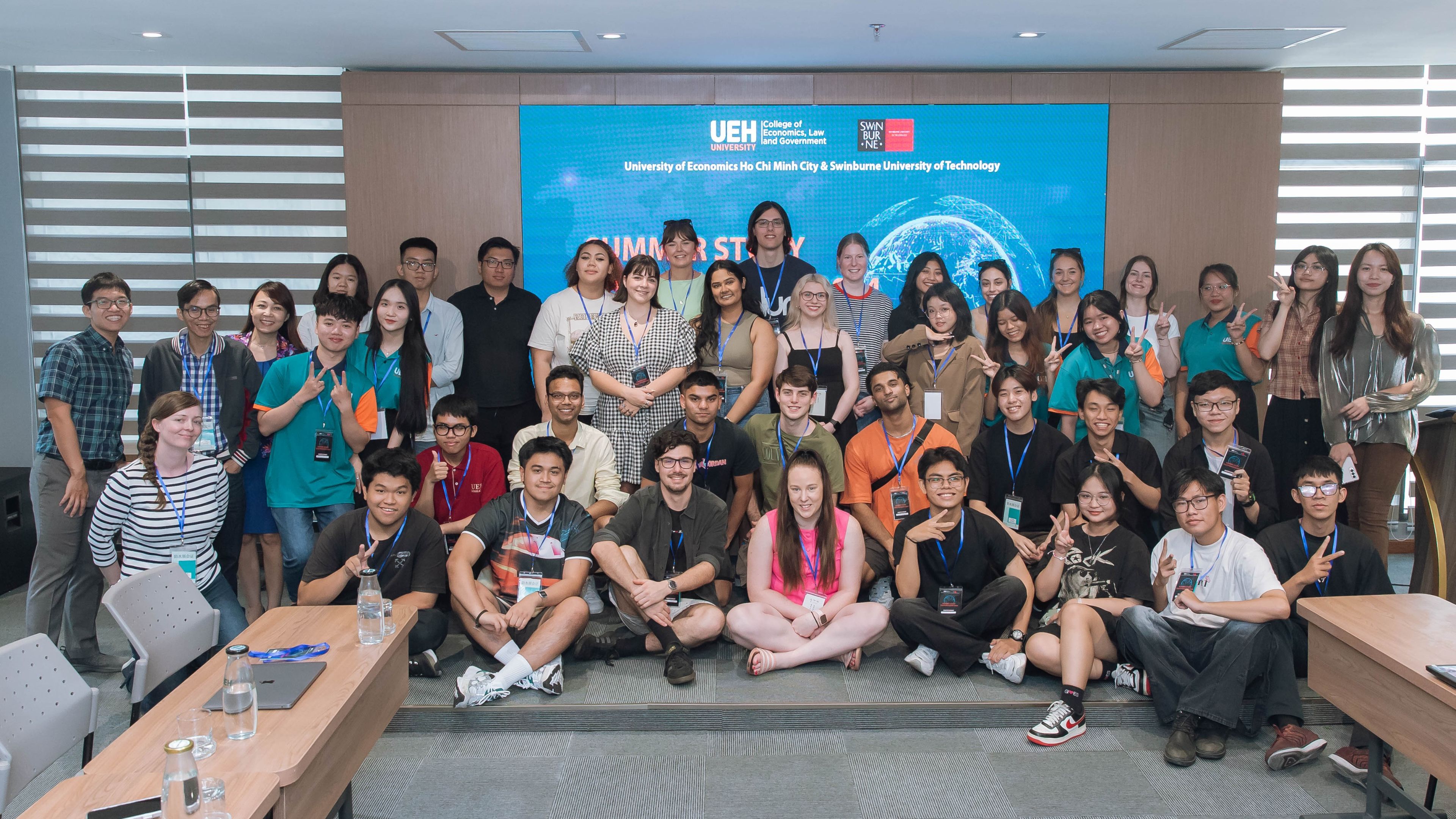 A large group of students and staff stand pose for a photo in an UEH classroom