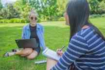 Two students do work online in the park under the shade of a tree
