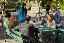 A group of students sit at a table outside chatting 