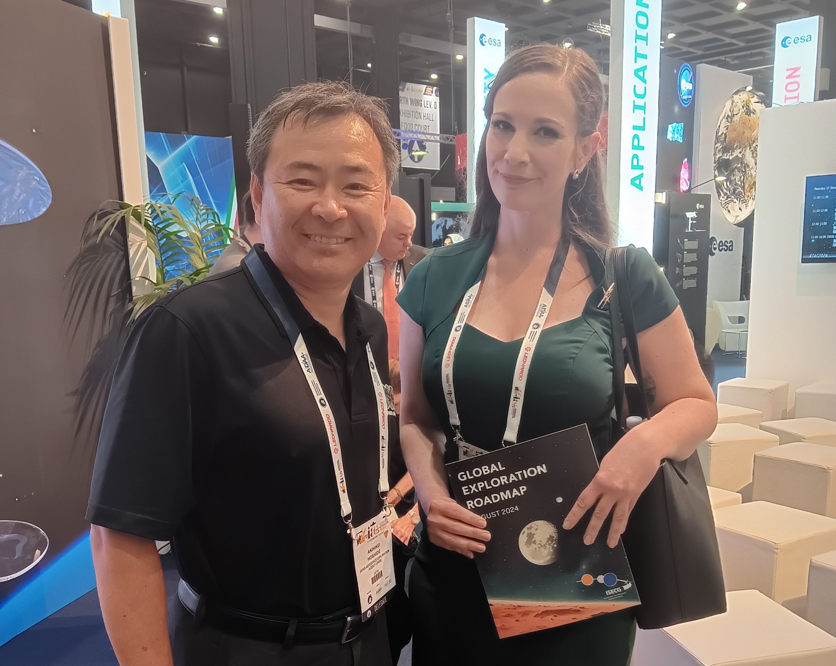 A women in a green dress poses beside a man in a black shirt. They are both smiling with lanyards around their necks 