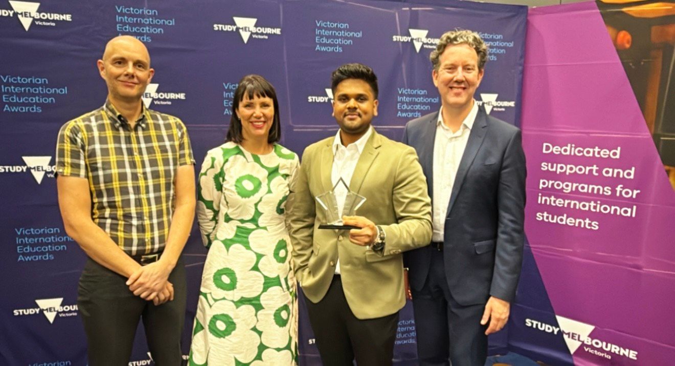 A group of four people pose in front of a purple background with Study Melbourne branding, one person holding an award