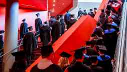 Students dress in graduation regalia line the steps as they wait to walk on stage
