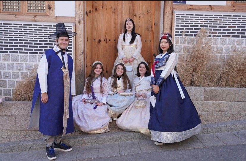 Henry Edwards on the left in traditional blue Korean hanbok posing with 5 other girls in hanbok