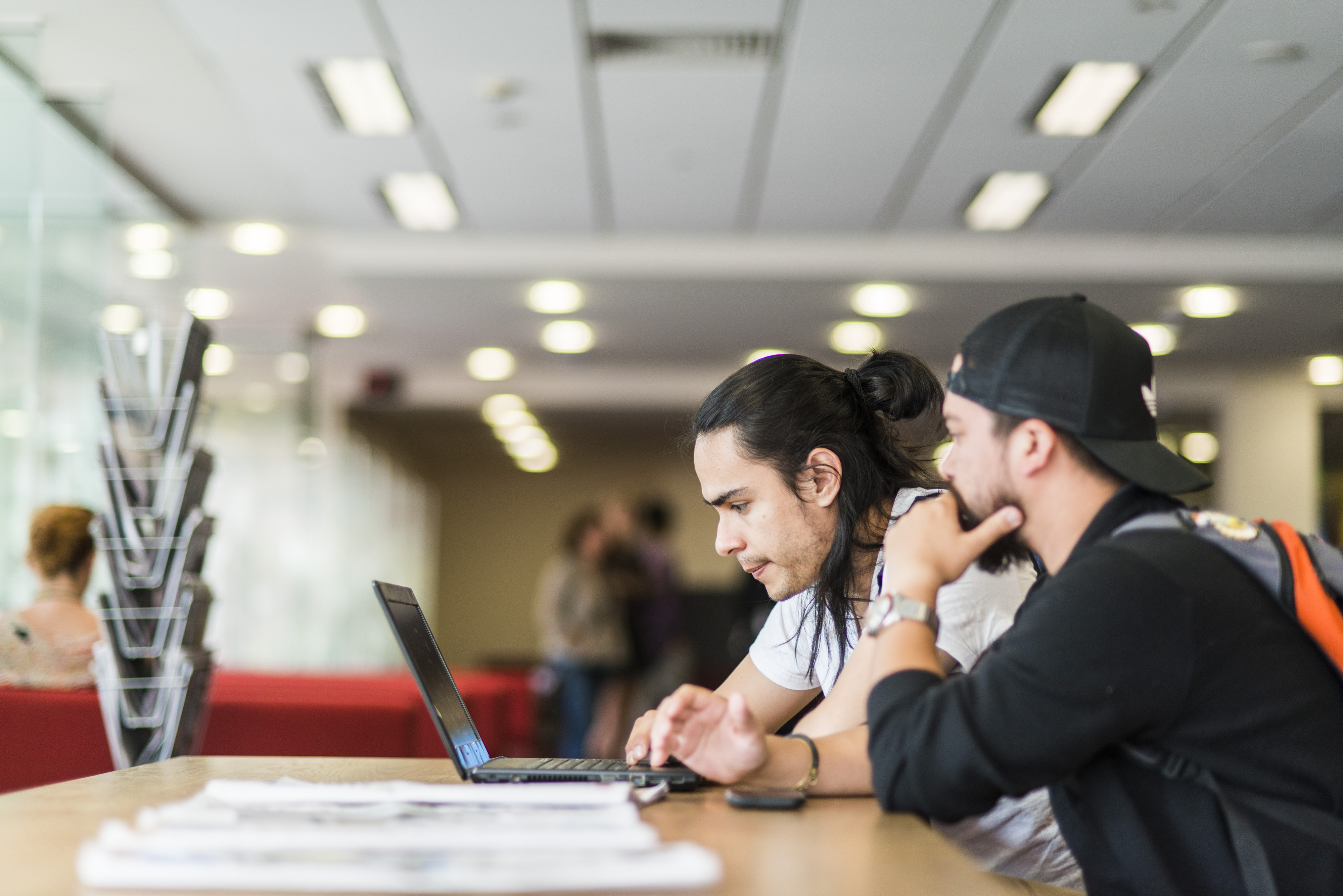 Two students sitting at a desk, looking at a laptop together.