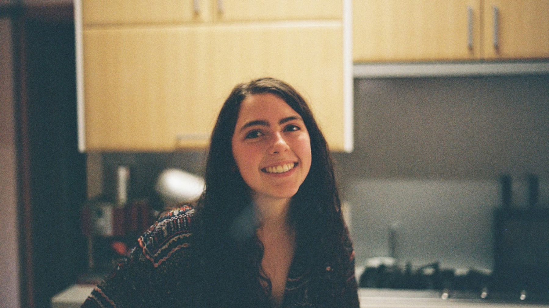 Claudia, a young female student with brown hair, standing and smiling in a kitchen.