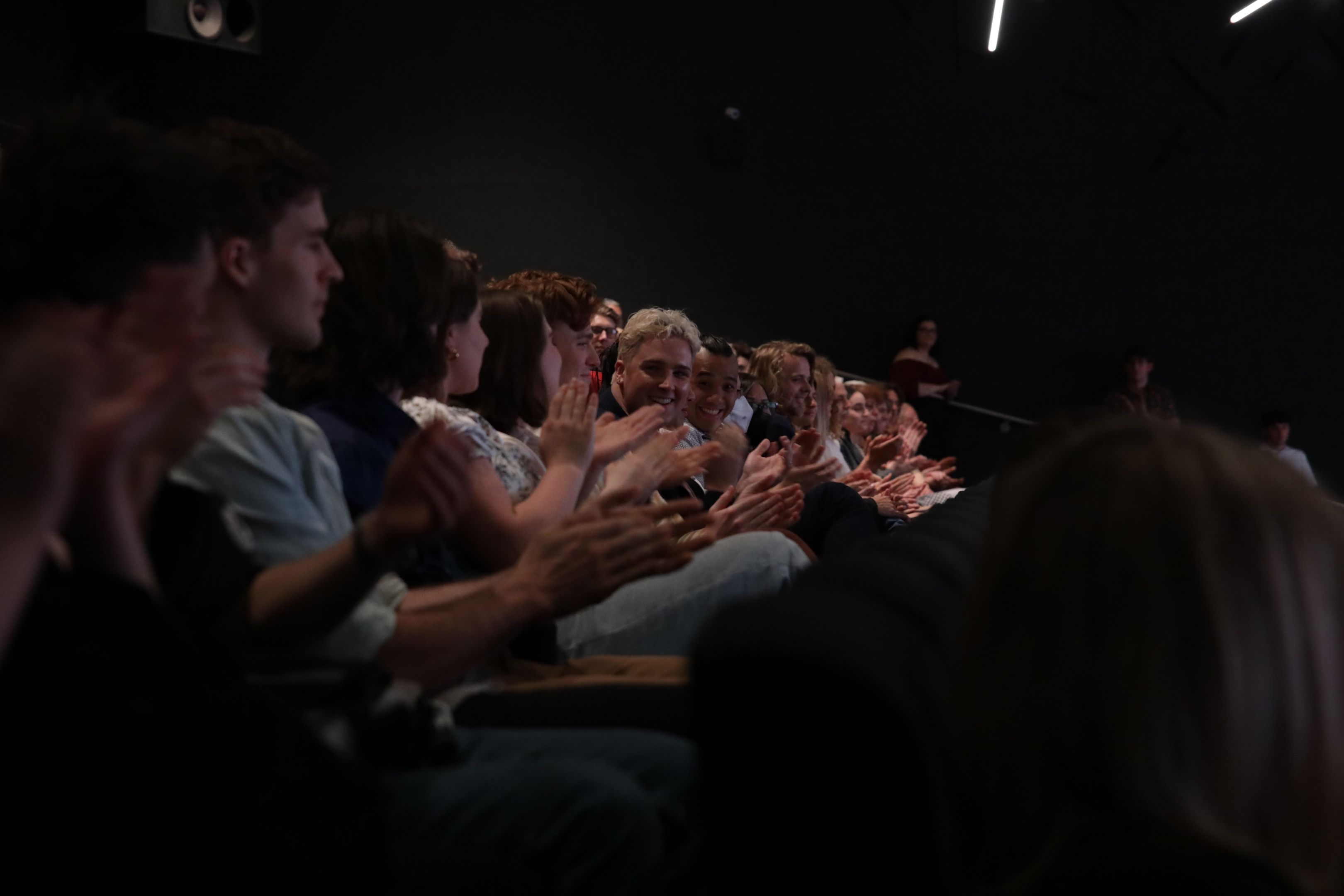 A theatre audience applauds in their seats