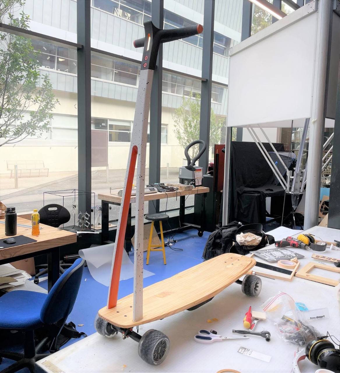 The prototype of the ark-e micro mobility design sits on a working desk in the protolab, it looks similar to a scooter but with a base and wheels like a cruiser skateboard