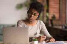 Focused mixed race woman wearing headphones watching webinar write notes