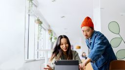 A casually dressed male student wearing beanie points at a laptop next to a female student. 